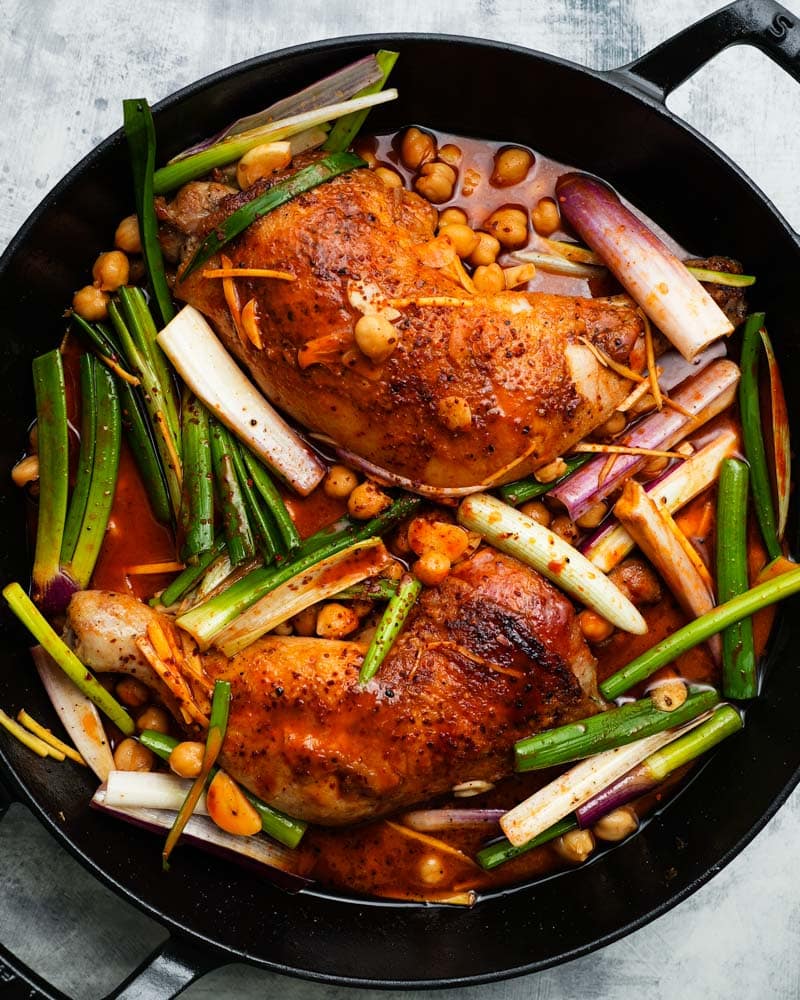 Gochujang glazed chicken with chickpeas and scallions in a black skillet.