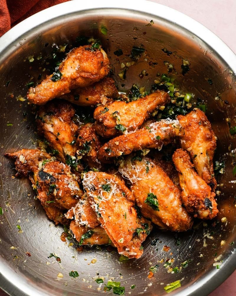 Crispy chicken wings tossed with garlic, parmesan, and green onions in a metal bowl.