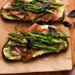 Asparagus tartine with ricotta, prosciutto, dill, and garnished with basil leaves on bread.