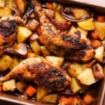 Roasted chicken legs with potatoes, carrots, and red onions in a baking tray.