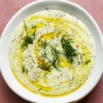 Herb whipped ricotta garnished with dill and olive oil in a white bowl.