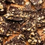 Matzo toffee topped with chocolate, hazelnuts, and sea salt on parchment paper.