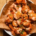 A bowl of crispy shrimp topped with creamy sauce and fresh chopped chives.