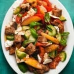 Colorful Peach Panzanella salad with feta, fresh vegetables, and torn bread on a plate.