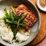 Salmon glazed with honey ginger atop rice, garnished with green onions and sesame seeds.