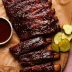 Barbecue ribs topped with sesame seeds, served with sauce and pickle slices.