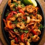 Colorful shrimp fajitas with bell peppers, onions, cilantro, and lime wedges.