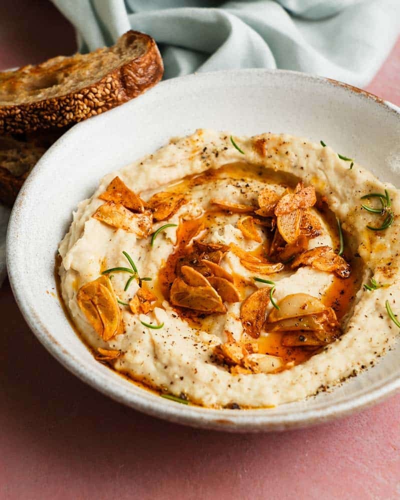 Creamy white bean dip with crispy garlic and rosemary garnished with oil.