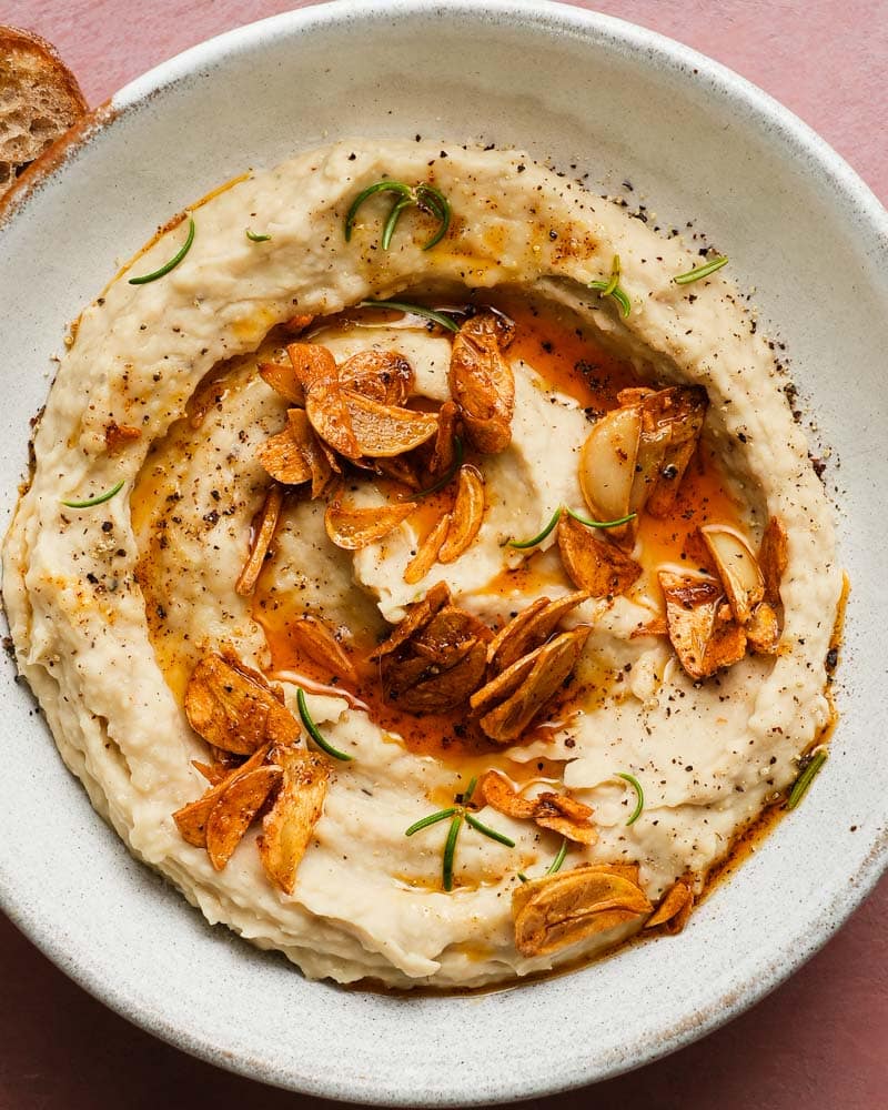 Creamy white bean dip topped with crispy garlic and rosemary in a bowl.
