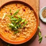 Bowl of creamy ramen topped with sliced green onions and chili flakes.