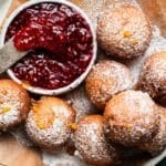 Golden ricotta fritters dusted with powdered sugar beside a bowl of raspberry sauce.