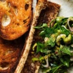 Toasted bread, seasoned roasted bone marrow, and vibrant parsley olive salad on a plate.