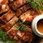 Sliced roasted turkey with rosemary and gravy in a white dish.