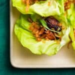 Lettuce wraps with miso-glazed black cod and crispy toppings on a square plate.