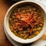 Bowl of Persian lentil soup topped with crispy fried onions on a wooden table.