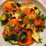 Sliced citrus and avocado with chili crisp and fresh mint on a ceramic plate.