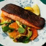 Crispy-skinned salmon served with citrus slices, avocado, and mint on a floral plate.
