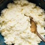 Homemade ricotta cheese in a blue bowl with a spoon.