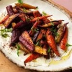 Roasted carrots with sumac and honey on ricotta, garnished with fresh herbs.