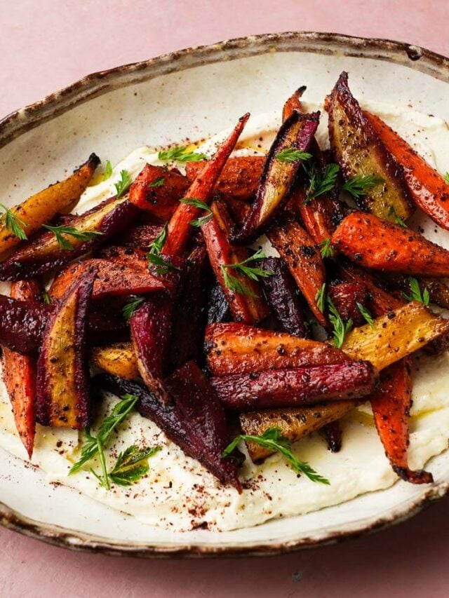Roasted carrots with sumac and honey on ricotta, garnished with fresh herbs.