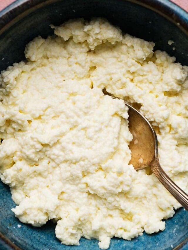 A bowl of creamy homemade ricotta cheese with a silver spoon.