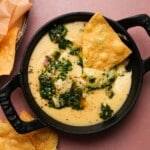 Black skillet of creamy queso garnished with herbs and tortilla chips.