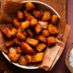 Bowl of crispy fried potatoes on brown paper, sprinkled with salt.