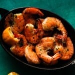 Grilled shrimp with basil butter and lemon in a black dish.