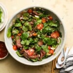 Bowl of Thai beef salad with greens, cherry tomatoes, and herbs.