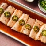Yellowtail sashimi topped with jalapeño slices in yuzu ponzu sauce on a plate.
