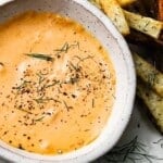 Saucer of chipotle mayo garnished with herbs and surrounded by fries.