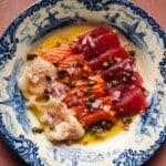 Colorful sashimi with capers and red onion on a decorative blue plate.