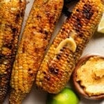 Grilled corn with Tajin lime butter, served with lime wedges and a butter dish.