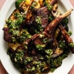 Grilled lamb chops topped with fresh herb sauce on a white plate.