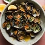 Bowl of steamed clams with herbs, lemon, and broth served in a gray bowl.
