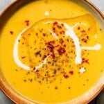 Bowl of creamy pumpkin soup garnished with cream, red pepper flakes, and pepper.