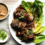 Korean short ribs garnished with scallions and sesame on a white plate with greens.