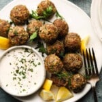 Lamb meatballs with herbs, lemon wedges, and a creamy dipping sauce on a plate.