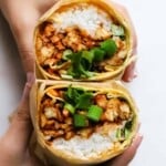 Two hands holding a KBBQ burrito cut in half, revealing ingredients inside.
