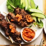 Grilled steak skewers with spicy sauce, garnished with cucumber slices and sesame seeds.