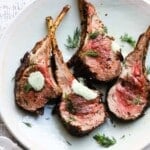 Grilled lamb chops with tzatziki sauce and fresh dill on a white plate.