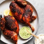 Grilled chicken with green dipping sauce, lemon slices, and sesame rice on a plate.