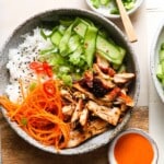 Bowl of chicken, rice, cucumbers, carrots, chili peppers, with a small orange sauce.