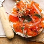 Bagel with cream cheese, gravlax, dill, red onion, and seasoning with a knife.