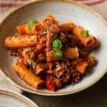 Bowl of rigatoni with spicy sausage, cherry tomatoes, and fresh basil topping.