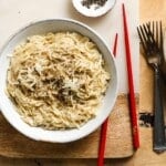 Bowl of cheesy miso ramen with grated cheese and pepper, red chopsticks nearby.