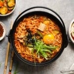 Bowl of kimchi ramen stew with egg, tofu, seaweed, and green onions.