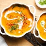 Creamy pumpkin carrot soup garnished with herbs and spices in white bowls.