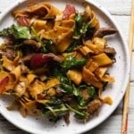 A plate of spicy Sichuan lamb noodles with vegetables and herbs.