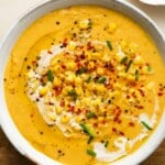 Creamy corn soup garnished with chives, chili flakes, and whole corn kernels.